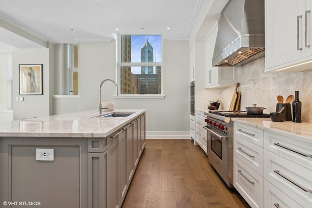 kitchen with a center island with sink, wall chimney exhaust hood, luxury range, and white cabinetry