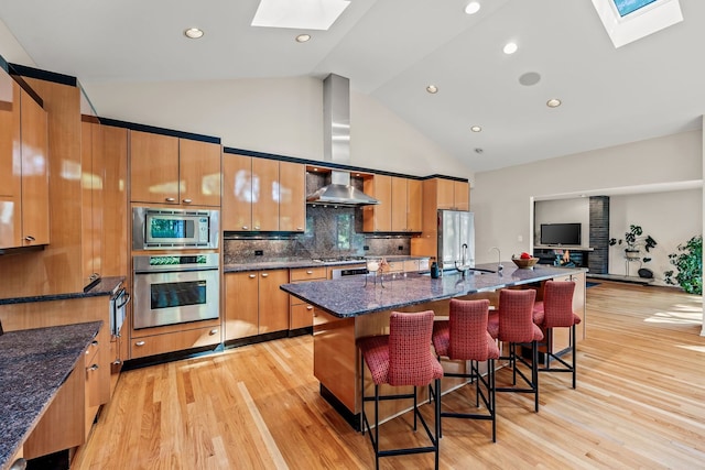 kitchen featuring high vaulted ceiling, stainless steel appliances, a skylight, and light hardwood / wood-style flooring