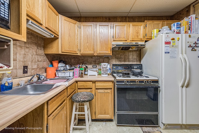 kitchen with a paneled ceiling, black gas stove, sink, and white fridge