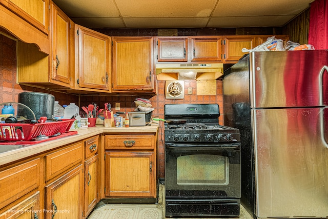 kitchen featuring black gas range oven, stainless steel refrigerator, and a drop ceiling