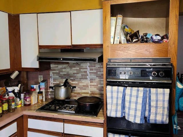 6926 S Vernon Ave, Chicago, IL 60637 - kitchen with white cabinets, gas cooktop, under cabinet range hood, black oven, and decorative backsplash