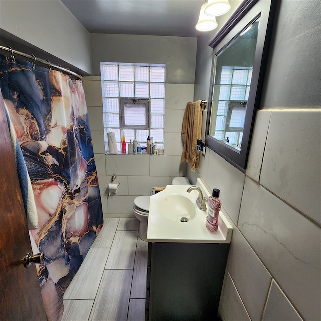 bathroom featuring vanity, toilet, a wealth of natural light, and tile walls