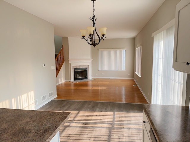 unfurnished living room featuring dark wood-type flooring, a tiled fireplace, and a chandelier