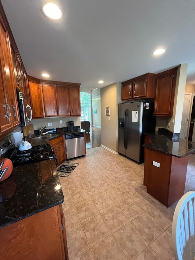 kitchen with sink, light tile patterned floors, appliances with stainless steel finishes, and dark stone counters