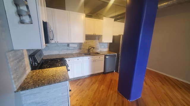 kitchen featuring appliances with stainless steel finishes, light hardwood / wood-style floors, sink, white cabinetry, and dark stone countertops