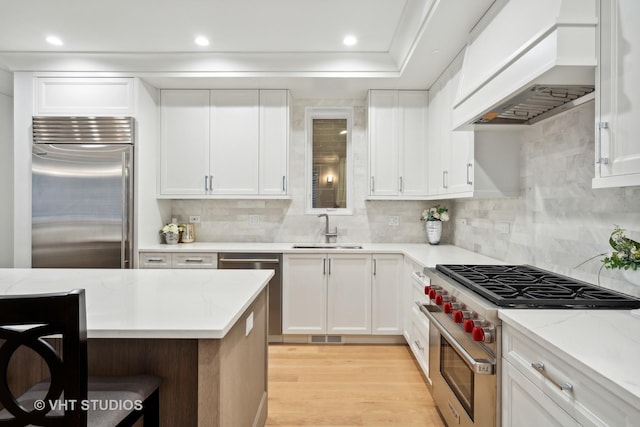 kitchen with high end appliances, sink, white cabinetry, and custom exhaust hood