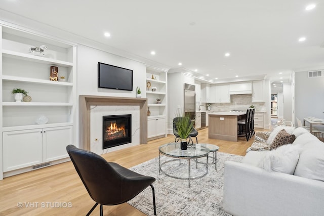 living room featuring a premium fireplace, ornamental molding, built in features, and light hardwood / wood-style floors