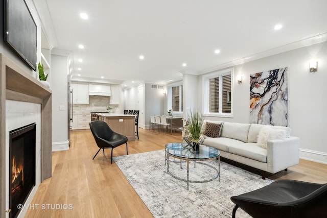 living room with crown molding, a premium fireplace, and light hardwood / wood-style floors