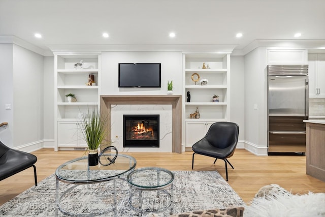 living room featuring built in shelves, a fireplace, ornamental molding, and light wood-type flooring