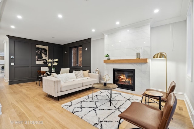 living room with a tile fireplace, ornamental molding, and light wood-type flooring