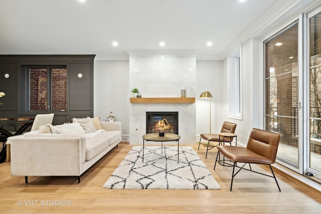 living room with a tile fireplace, ornamental molding, and light hardwood / wood-style floors