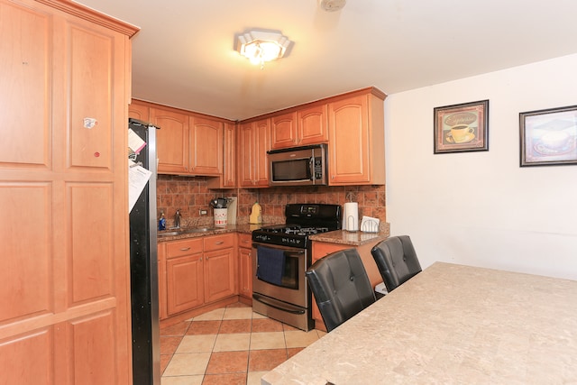 kitchen with appliances with stainless steel finishes, decorative backsplash, stone counters, and light tile patterned flooring