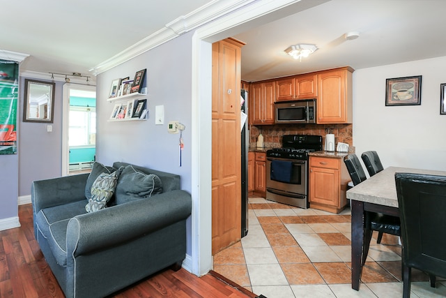 kitchen featuring crown molding, light hardwood / wood-style flooring, appliances with stainless steel finishes, and decorative backsplash