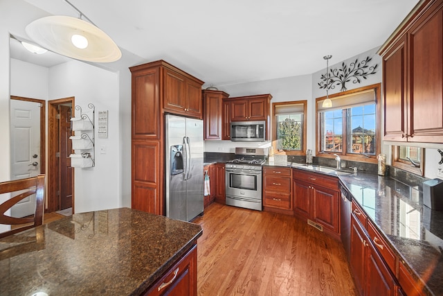 kitchen with hanging light fixtures, light wood-type flooring, dark stone countertops, stainless steel appliances, and sink