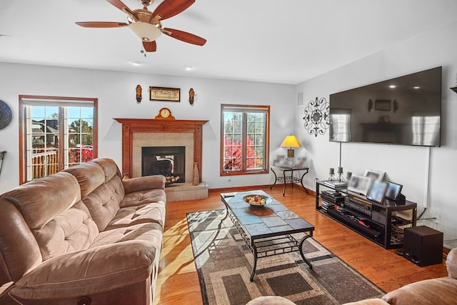 living room with a tiled fireplace, light hardwood / wood-style floors, and ceiling fan