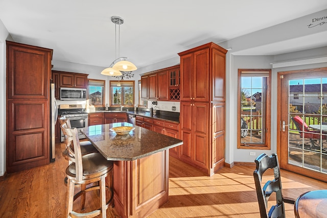 kitchen featuring dark stone counters, a center island, pendant lighting, appliances with stainless steel finishes, and light hardwood / wood-style floors