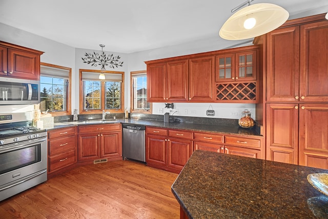 kitchen featuring appliances with stainless steel finishes, light hardwood / wood-style flooring, decorative light fixtures, and dark stone counters