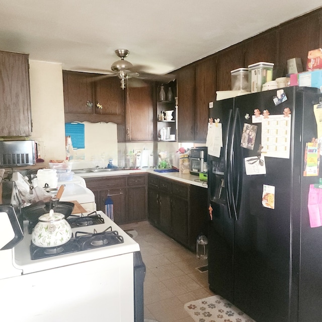 kitchen featuring white range with gas stovetop, dark brown cabinets, black fridge with ice dispenser, ceiling fan, and light tile patterned flooring