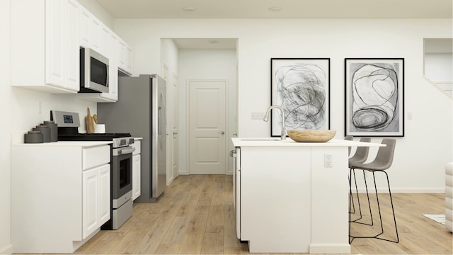 kitchen with a kitchen breakfast bar, appliances with stainless steel finishes, sink, white cabinets, and light hardwood / wood-style floors