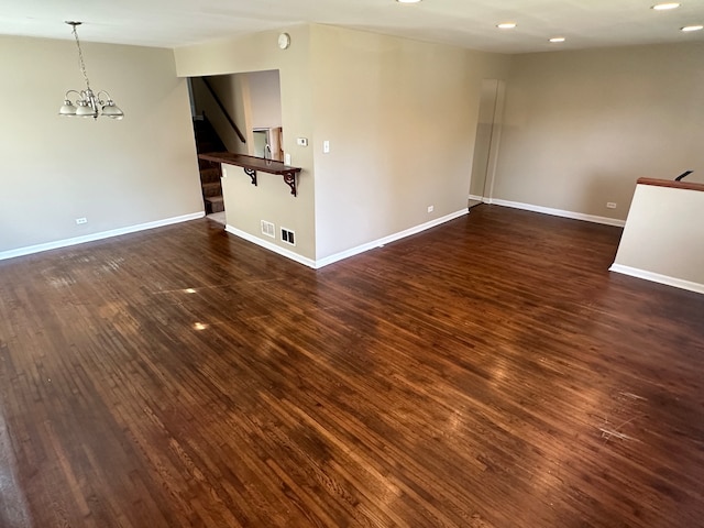 empty room with a notable chandelier and dark hardwood / wood-style flooring