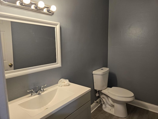 bathroom with toilet, vanity, baseboards, and wood finished floors