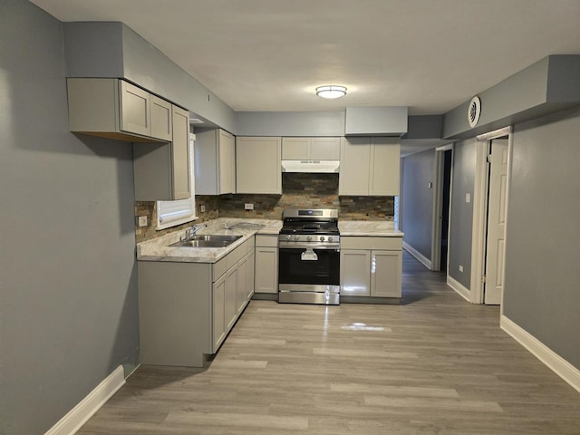 kitchen featuring light wood finished floors, stainless steel gas stove, under cabinet range hood, and a sink
