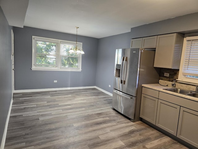 kitchen with stainless steel refrigerator with ice dispenser, a sink, light wood finished floors, baseboards, and a chandelier