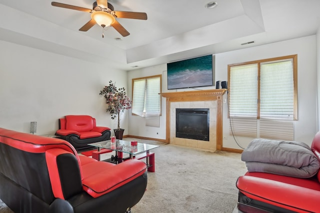 carpeted living room featuring ceiling fan, a tiled fireplace, and a raised ceiling