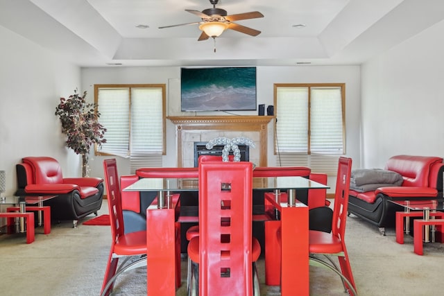 dining area with a raised ceiling, ceiling fan, a tiled fireplace, and carpet flooring