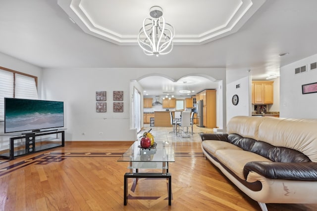 living room featuring a raised ceiling, an inviting chandelier, and light wood-type flooring