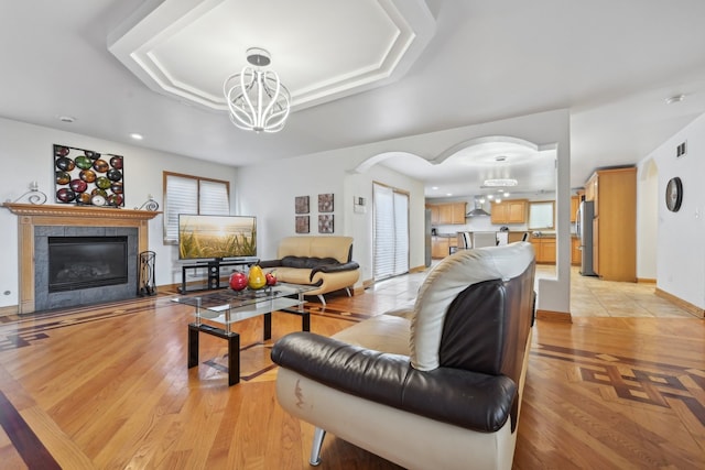 living room featuring light wood-type flooring, a tray ceiling, a fireplace, and an inviting chandelier