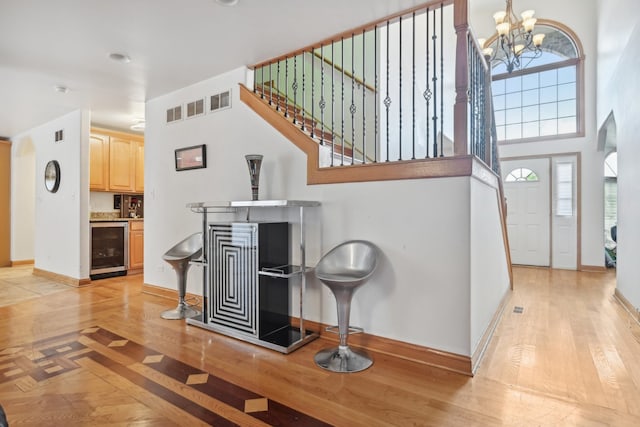 interior space featuring a towering ceiling, a chandelier, hardwood / wood-style floors, and wine cooler