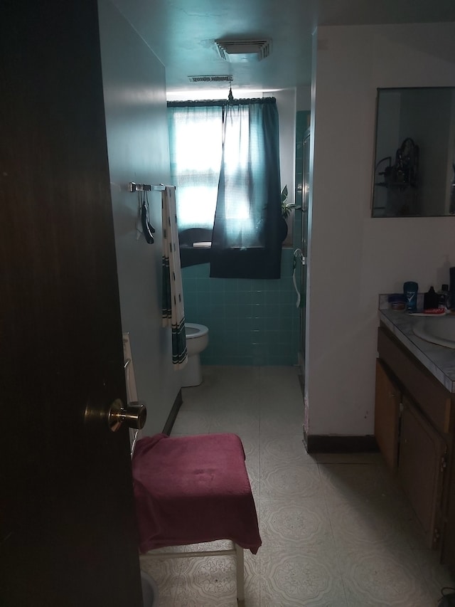 bathroom with tile walls, vanity, a shower, and toilet