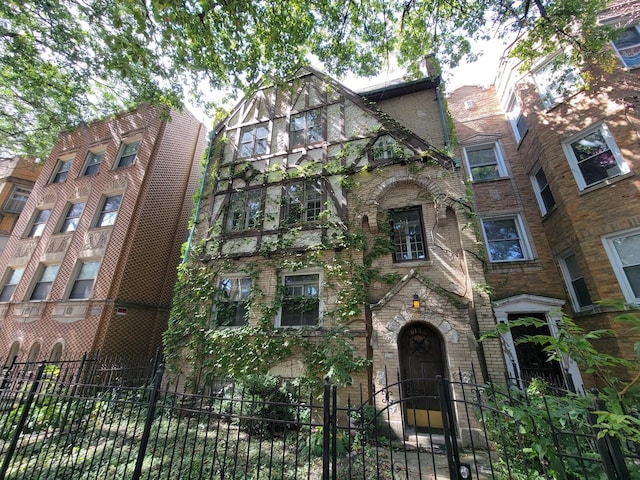 tudor-style house featuring a fenced front yard and brick siding