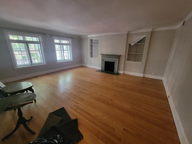 unfurnished living room with crown molding, a fireplace with flush hearth, wood finished floors, built in features, and baseboards