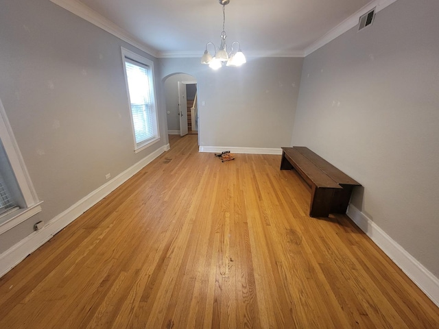 unfurnished dining area featuring visible vents, light wood finished floors, baseboards, ornamental molding, and arched walkways
