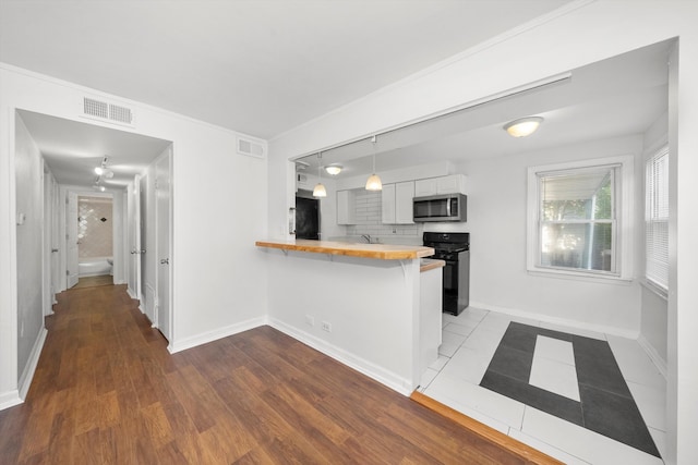 kitchen featuring pendant lighting, light hardwood / wood-style flooring, black stove, a kitchen bar, and kitchen peninsula