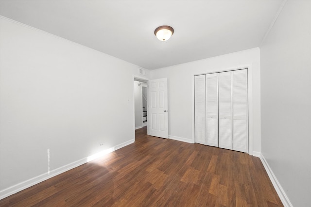 unfurnished bedroom with a closet, dark hardwood / wood-style floors, and crown molding