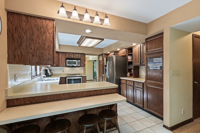 kitchen with backsplash, appliances with stainless steel finishes, a kitchen bar, kitchen peninsula, and sink