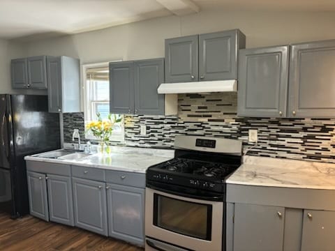 kitchen with stainless steel range with gas stovetop, gray cabinetry, dark hardwood / wood-style floors, and backsplash