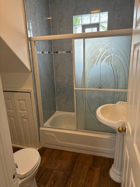 bathroom featuring enclosed tub / shower combo, toilet, and hardwood / wood-style flooring