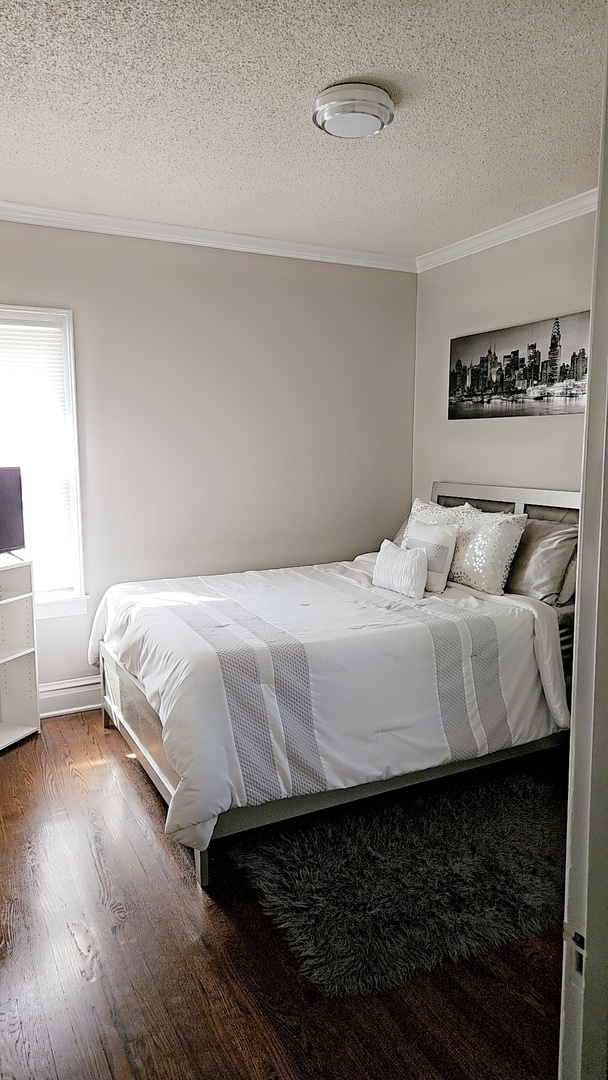 bedroom with a textured ceiling, crown molding, and dark hardwood / wood-style flooring