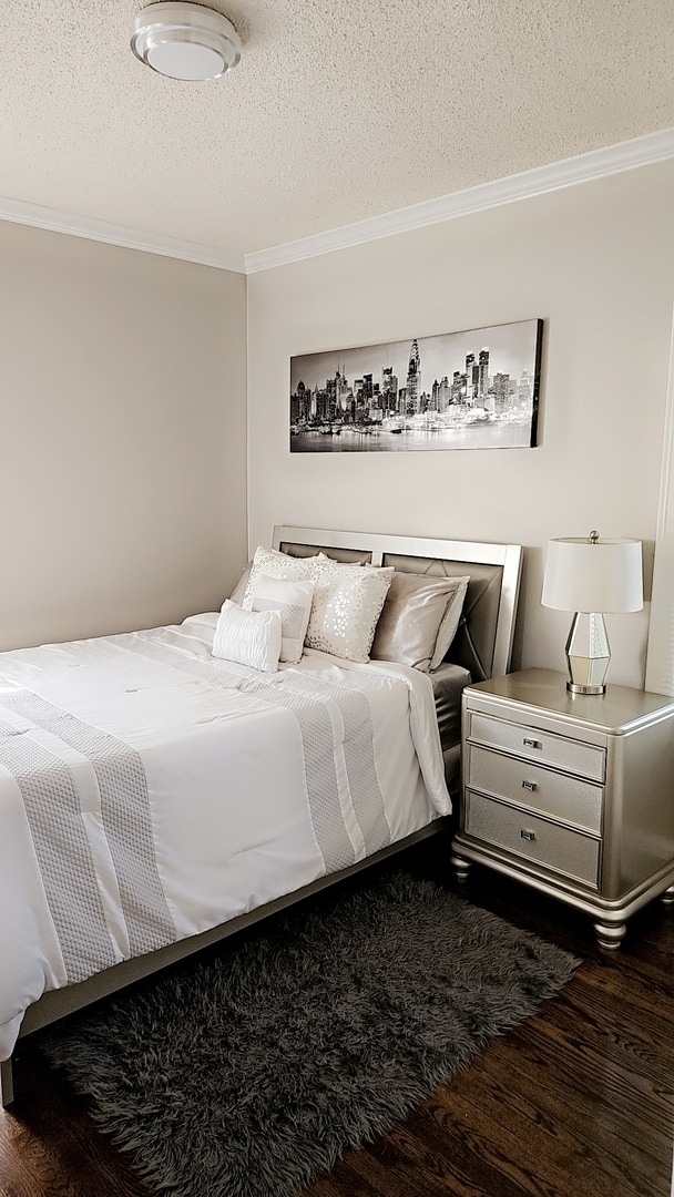 bedroom with a textured ceiling, crown molding, and dark hardwood / wood-style flooring