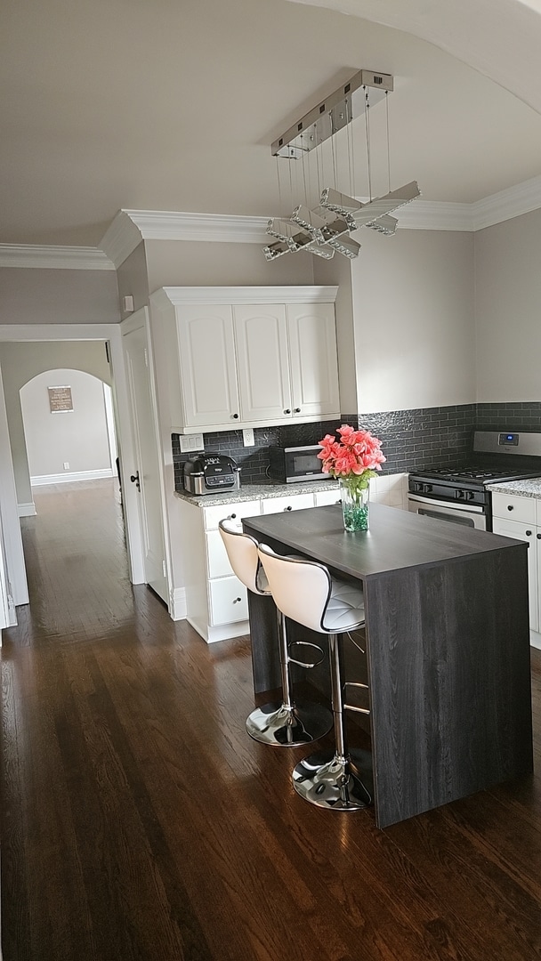 kitchen featuring stainless steel stove, white cabinetry, tasteful backsplash, and a center island