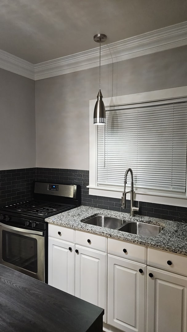 kitchen with pendant lighting, crown molding, gas stove, sink, and white cabinets