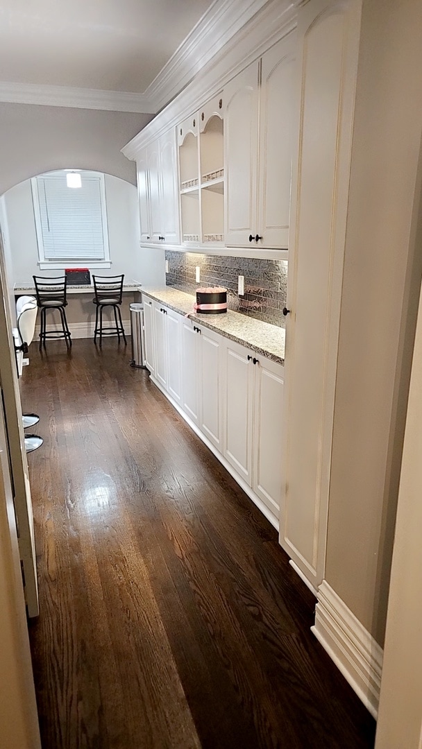 kitchen featuring tasteful backsplash, crown molding, dark hardwood / wood-style flooring, light stone counters, and white cabinets