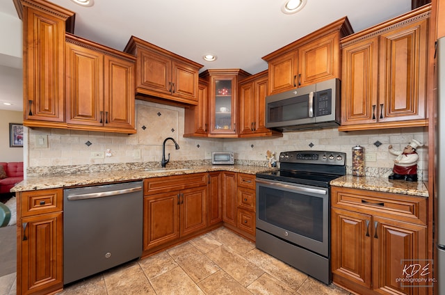 kitchen with decorative backsplash, stainless steel appliances, light stone counters, and sink