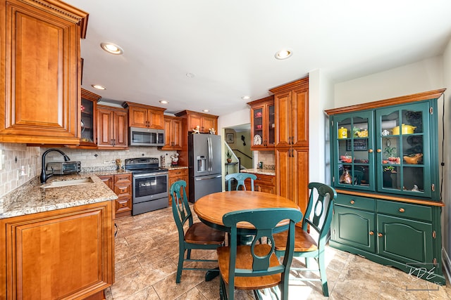 kitchen with light stone counters, appliances with stainless steel finishes, tasteful backsplash, and sink