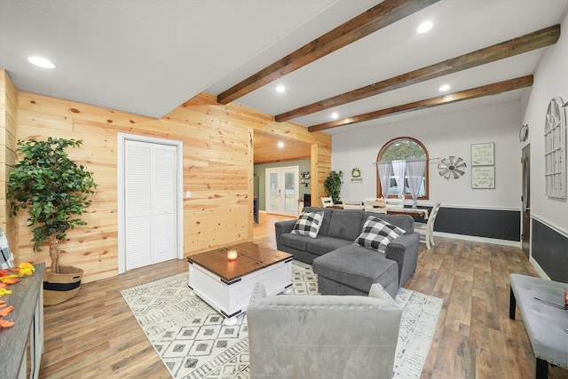 living room featuring beamed ceiling, french doors, light wood-type flooring, and wooden walls