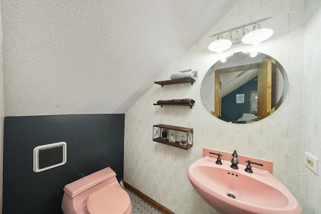 bathroom featuring a textured ceiling, toilet, lofted ceiling, and sink